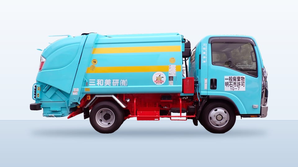 小型のパッカー車の側面。水色の車体に黄色の帯が入っている。